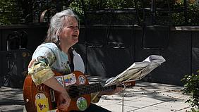 Maria Haug Rakos sitzt vor dem Seniorenheim und singt. Dabei spielt sie auf einer Gitarre